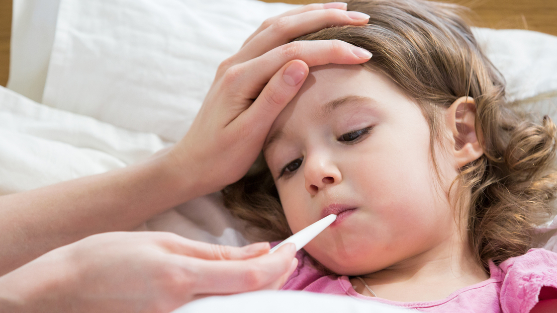 Mother measuring temperature of her ill kid. Sick child with high fever laying in bed and mother holding thermometer. Hand on forehead.