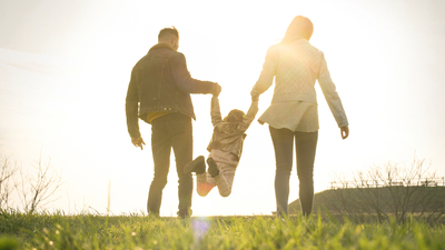 Happy parents playing with their daughter in the park. Space for copy. From behind.