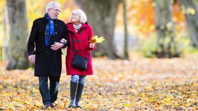 Senior couple are walking together through the autumn woods. The woman is arm in arm with her husband and is carrying leaves.