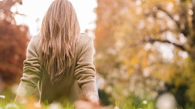 woman is sitting on the grass in public park