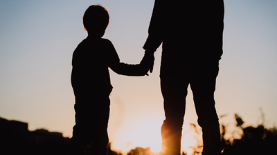 silhouette of father and son holding hands at sunset sky