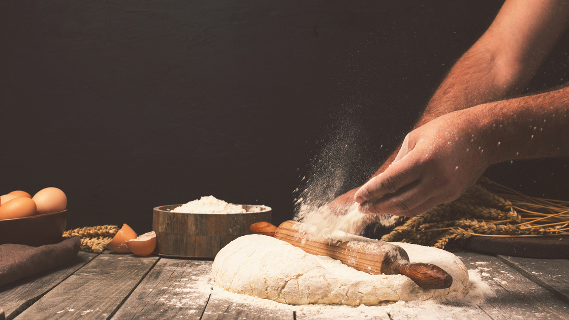Men hands sprinkle a dough with flour close up. Man preparing bread dough