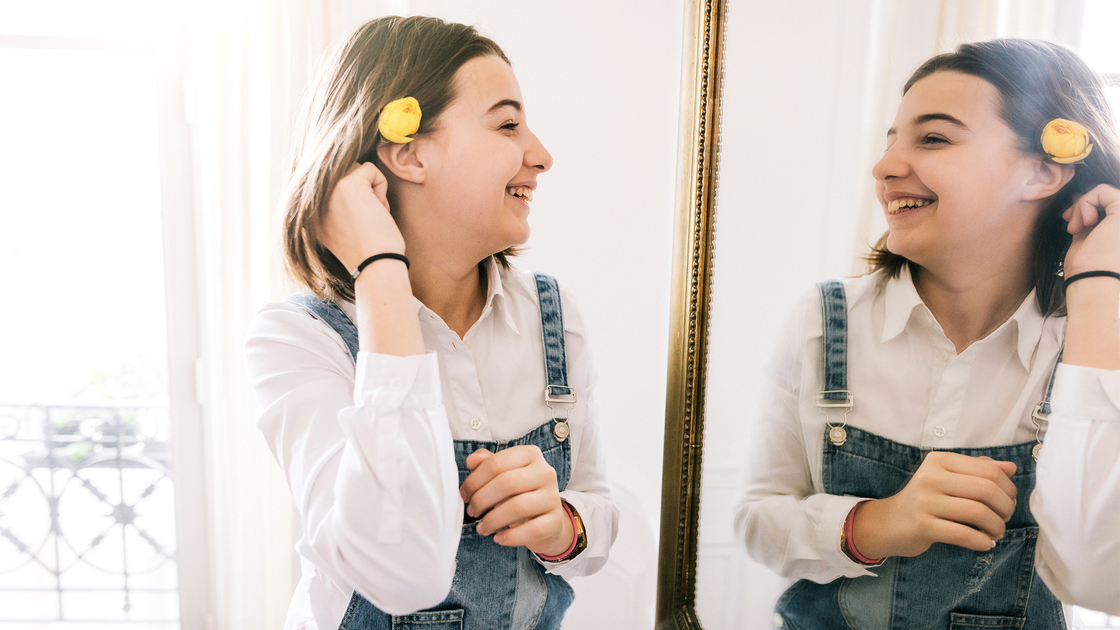 Teenage girl with flower looking into the mirror 