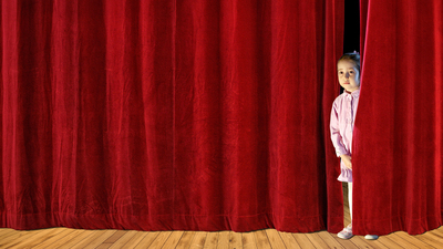 little shy girl looking behind red curtain on stage