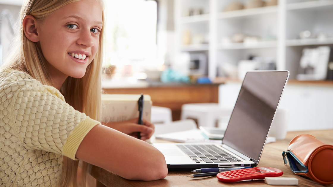 Girl using laptop computer at home, smiling to camera