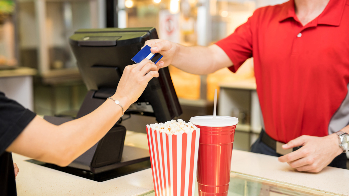 Closeup of a young woman handing over her credit card to pay for some snacks at the concession stand in a movie theater, fundraiser, 16x9