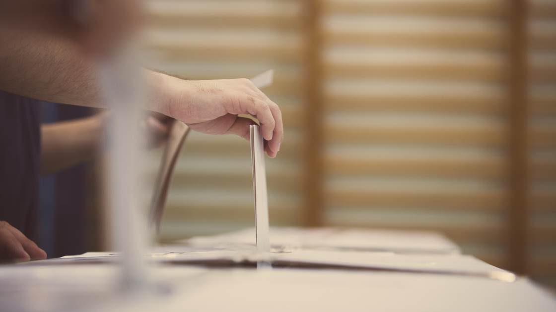 Hand of a person casting a ballot at a polling station during voting.