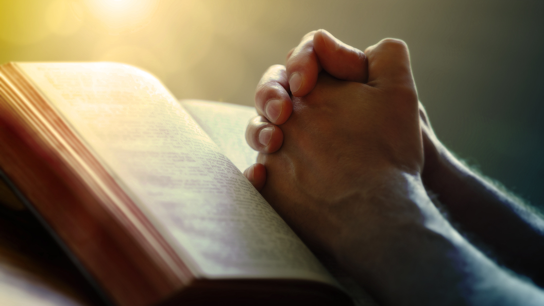 Hands folded in prayer on a Holy Bible in church concept for faith, spirtuality and religion