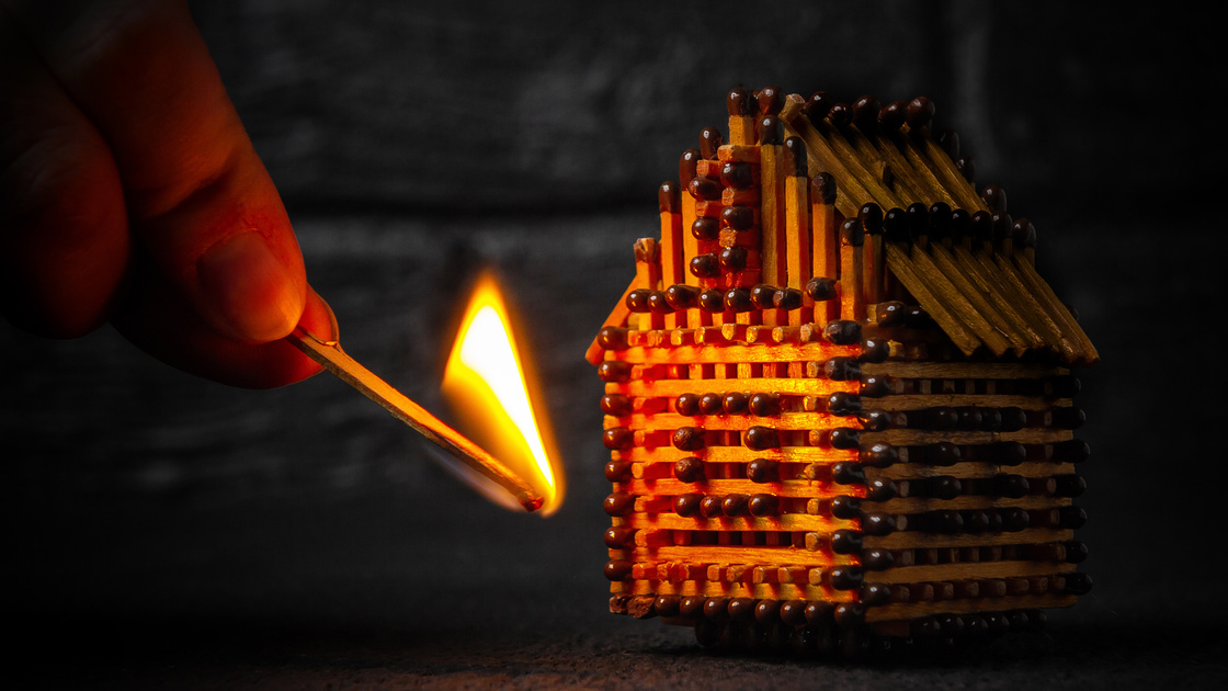 hand with a burning match sets fire to the house model of matches, risk, property Insurance protection or ignition of combustible materials concept.