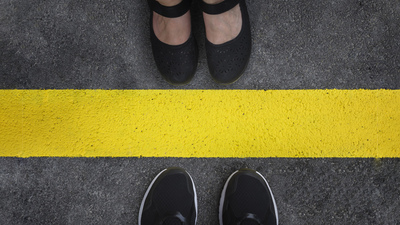 Legs of a couple standing opposite each other divided by the yellow asphalt line top view