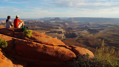 Couple sitting at the Green River Overview looking down into the valley carved by the Colorado and Green River. Canyonlands National Park, Utah, USA