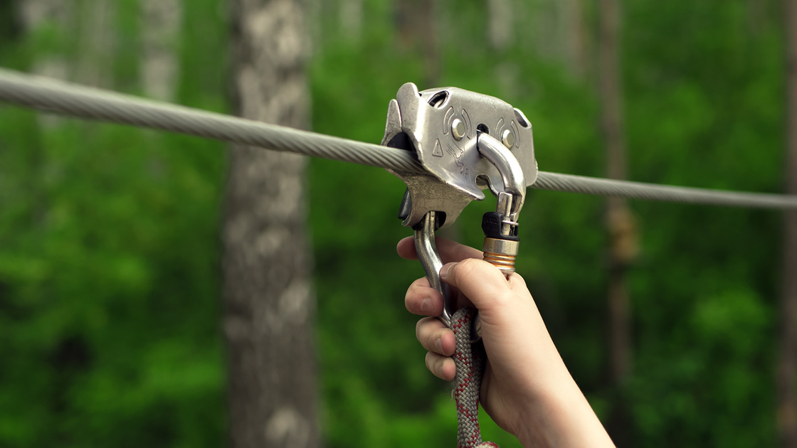 Zip line activity. Hands holding carabiner on zip line in forest.