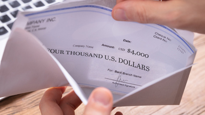 Elevated View Of Person's Hand Removing Paycheck From The Envelope Over Wooden Desk