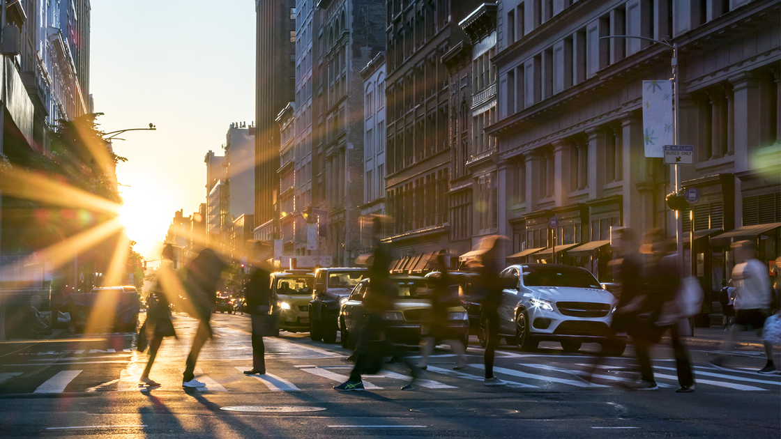 Rays of sunlight shine on the busy people walking across an intersection in Midtown Manhattan in New York City NYC