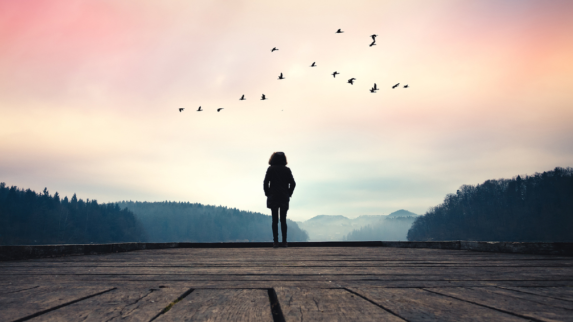 Woman standing on jetty and watching sunrise by the lake.