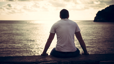 Rear view of lonely man looking with hope at horizon with sunlight during sunset with effect of light at the end of tunnel