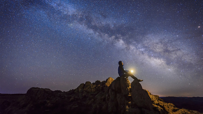 Man sitting under The Milky Way Galaxy with light on his hands.