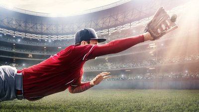 Outfielder baseball player about to catch ball during baseball game on outdoor baseball stadium under dramatic stormy skies.