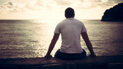 Rear view of lonely man looking with hope at horizon with sunlight during sunset with effect of light at the end of tunnel