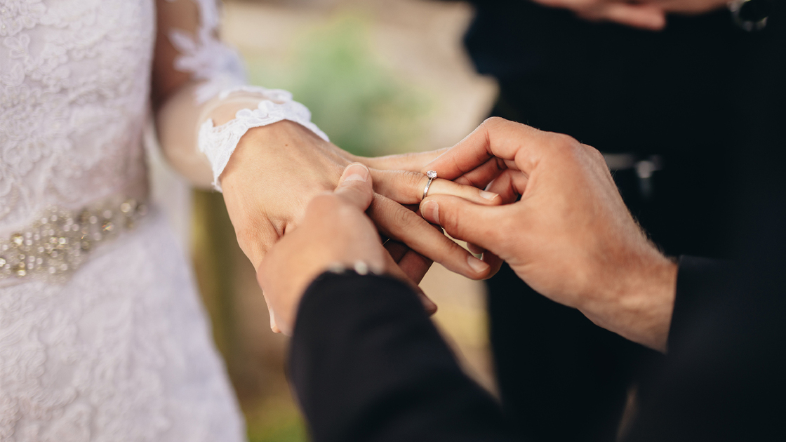 Closeup of groom placing a wedding ring on the brides hand.  Couple exchanging wedding rings during a wedding ceremony outdoors.