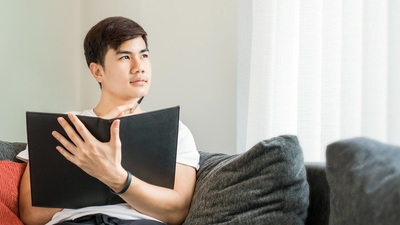 Asian Young Man Thinking and Wondering While Writing a Paper at Home