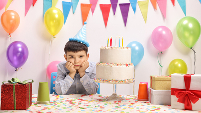 Sad and lonely little boy with a party hat and a birthday cake