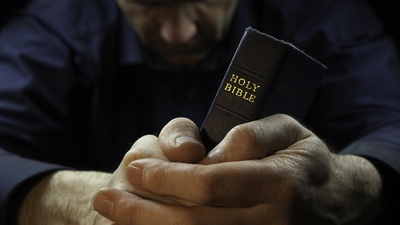 Man praying while holding a Holy Bible.