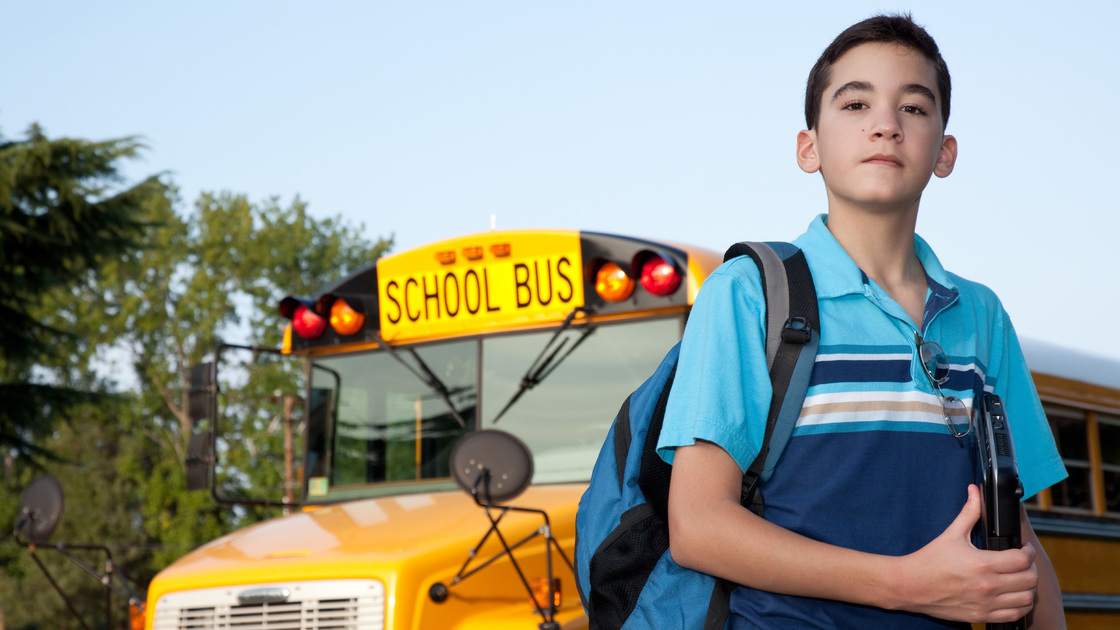 A young hispanic teen in front of the school bus.