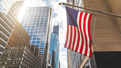 USA flag in Chicago with with skyscrapers on background. American flag waving in the city on a sunny day. Clouds reflections on buildings facade