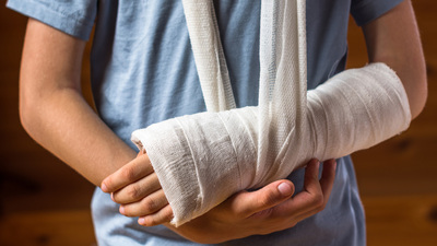 Boy with an arm in plaster indoors on the brown background , careless behavior at home, being in hospital, injury and health concept