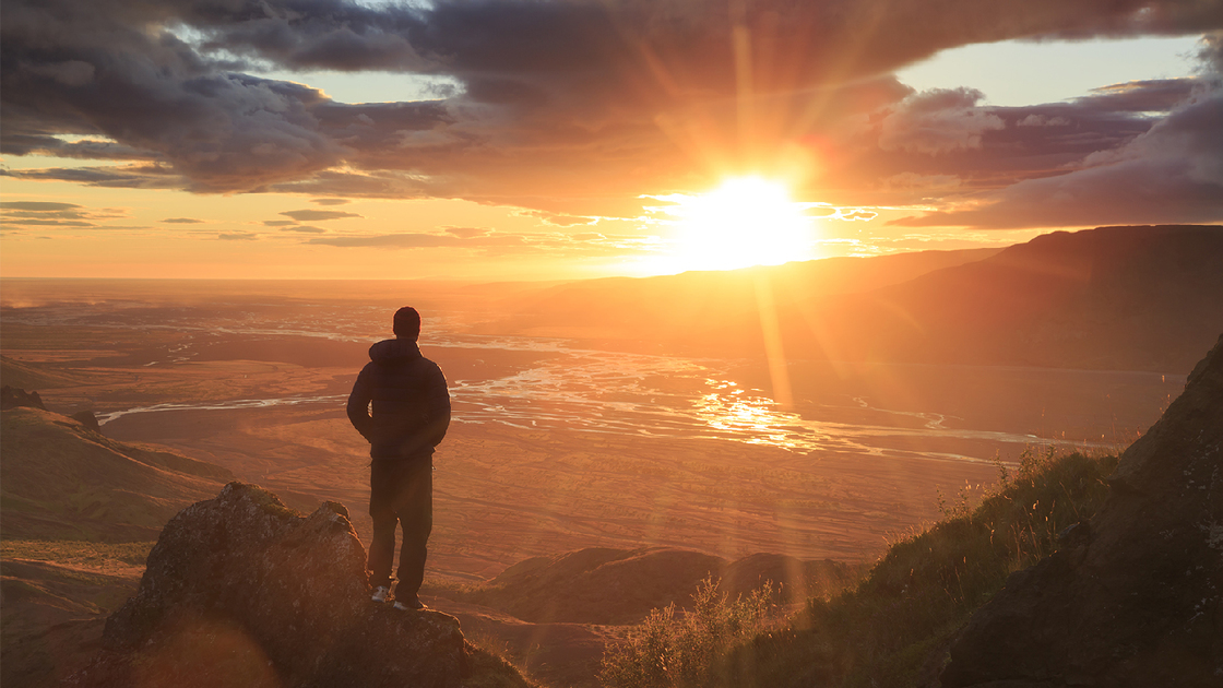 Man standing on a ledge of a mountain, enjoying the sunset over a river valley in Thorsmork, Iceland. With lens flare.