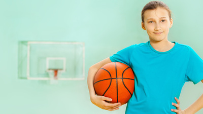 Portrait of happy 12 years old girl, basketball player, standing with ball in sports hall