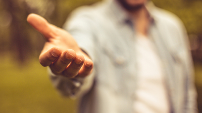 I'm always here to provide support. Young man in standing in park stretches his hand. Focus is on hand. Close up.