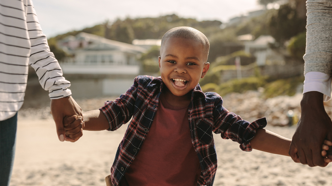 Smiling boy holding hands of father and mother on the beach. Family walking along the beach.