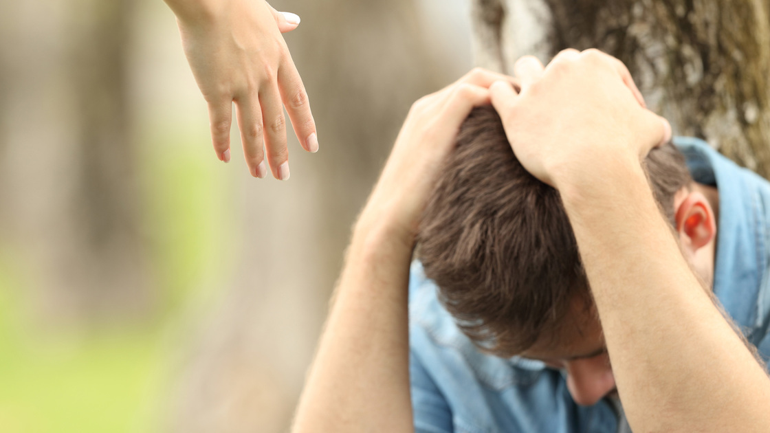 Sad teen sitting on the grass in a park and a woman hand offering help with a green background