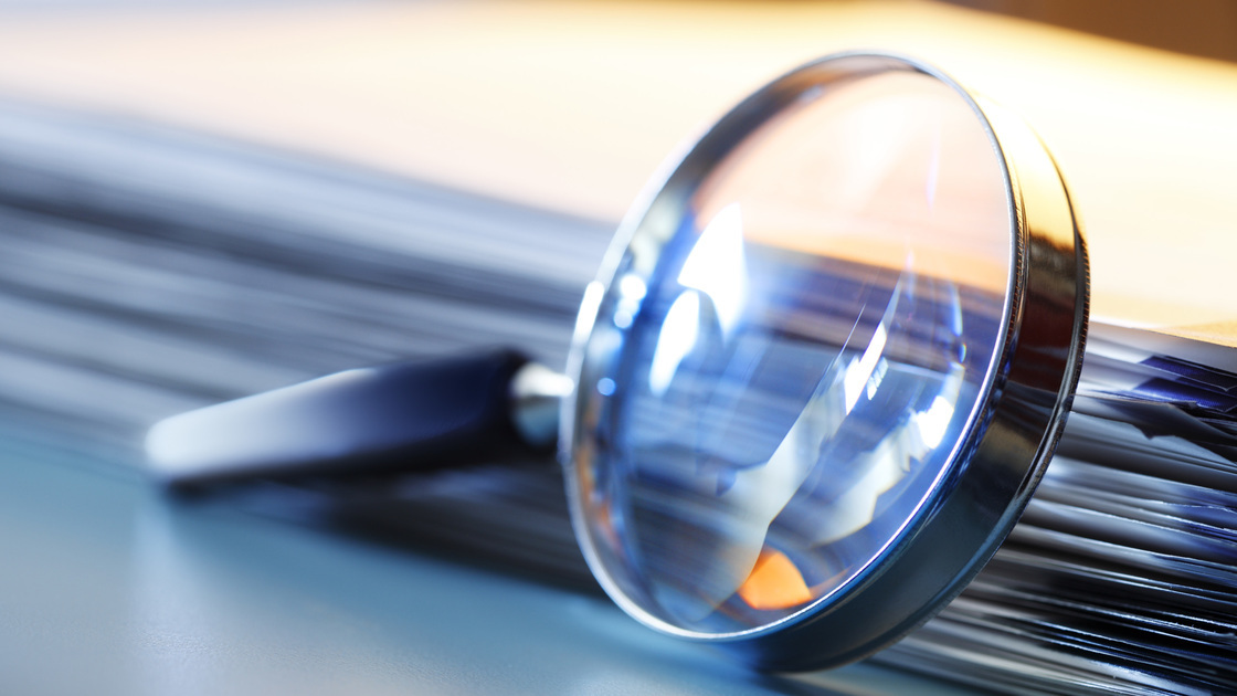 A magnifying glass leans against a thick stack of papers. Photographed with a very shallow depth of field.