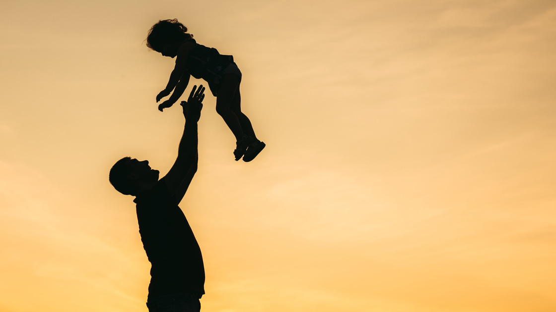 Father throwing his daughter in the air at sunset.