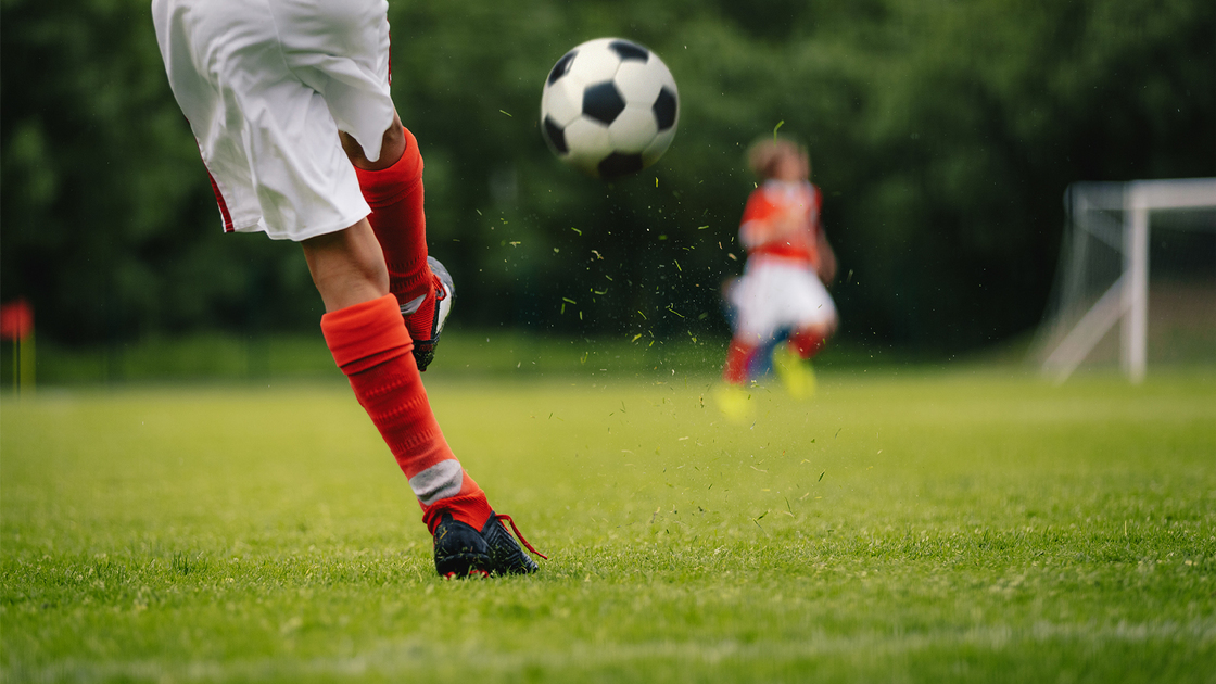 Football Kick. Youth Player Kicking Soccer Ball on Field. Football Ball in Motion. Legs of Sports Soccer Football Player Sportsman In Motion With Ball