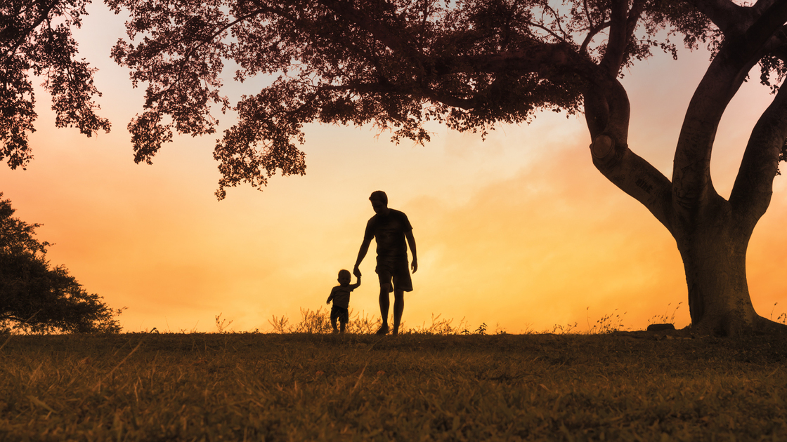 Father walking together with his little boy outdoors at sunset