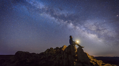 Man sitting under The Milky Way Galaxy with light on his hands.