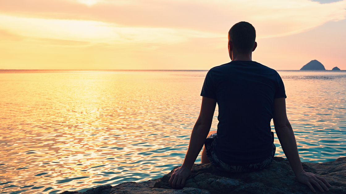 Contemplation at the beautiful sunset. Silhouette of the young man on the beach.