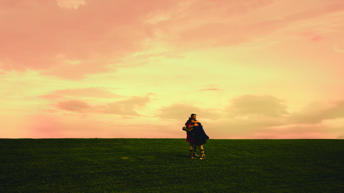 David (Micah Turgeon) hugs Jonathan (Cole March) in a well-manicured field with a pink sky.
