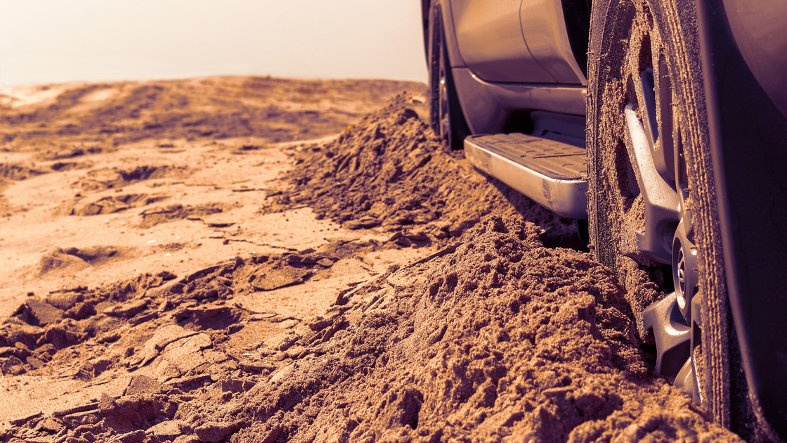 Car wheels on a sea beach sand. Close-up of car wheel on sandy dunes. Car stuck in the sand. Spinning wheel of a car stuck in the sand.