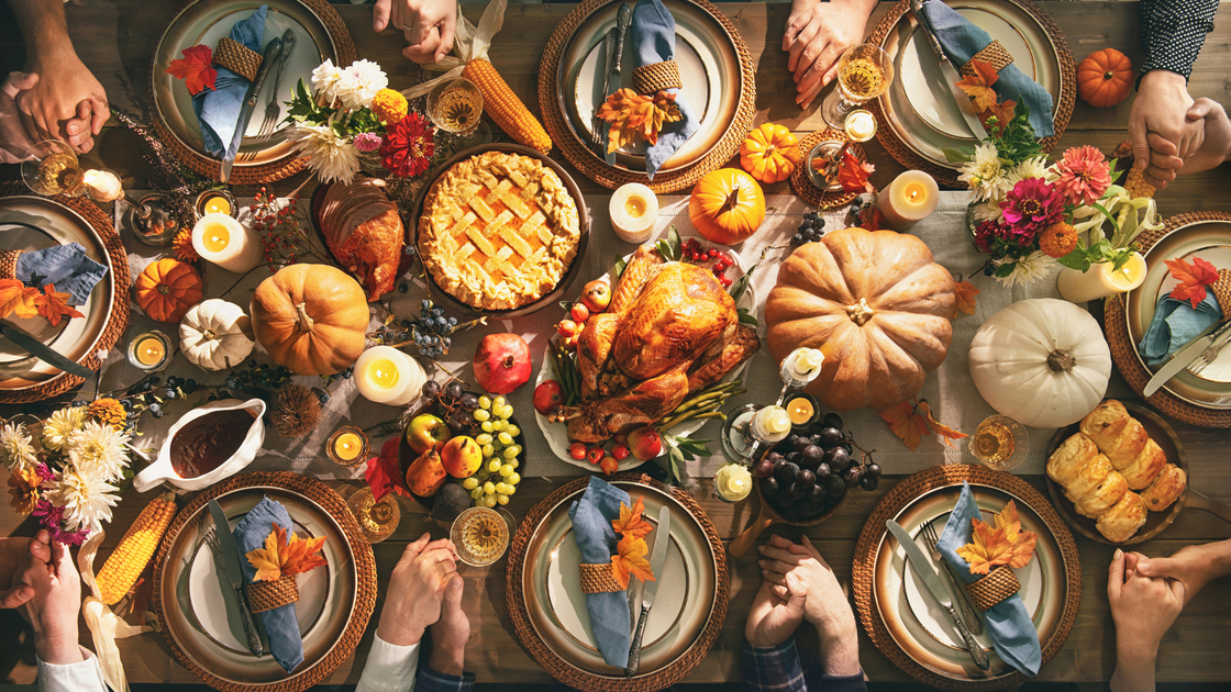 Group of friends or family members giving thanks to God at festive turkey dinner table together. Thanksgiving celebration traditional dinner concept