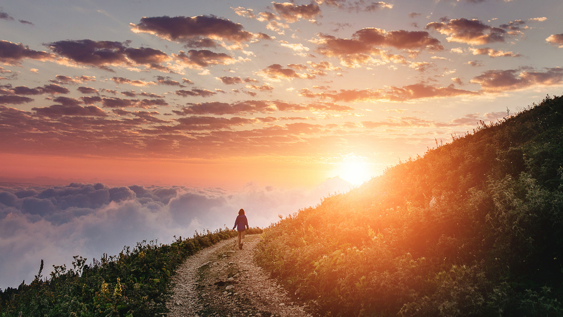 Woman on trail admiring the sunset with clouds and fog.