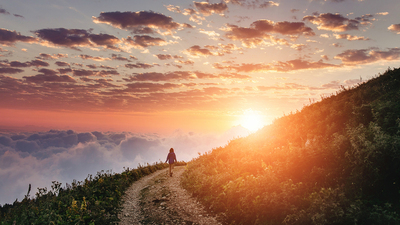 Woman on trail admiring the sunset with clouds and fog.