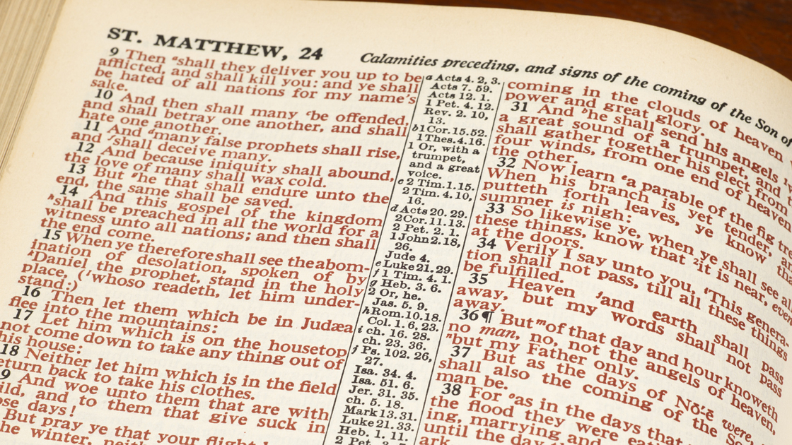 Horizontal close-up shot of an open Bible show Matthew 24 in red print.