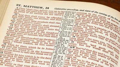 Horizontal close-up shot of an open Bible show Matthew 24 in red print.