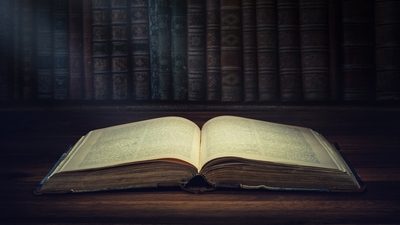 Open old book on a bookshelf background and the rays of light. Selective focus. Conceptual background on history, education, literature topics.