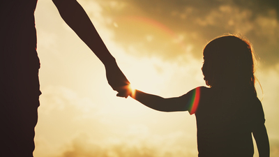 silhouette of little girl holding parent hand at sunset sky